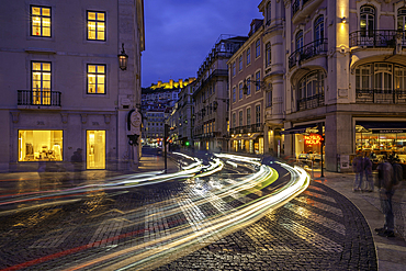 View of shops, car trail lights and Lisbon Castle at dusk, Lisbon, Portugal, Europe