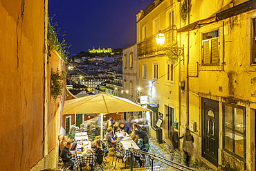 View of cafe and restaurant and steps with Lisbon Castle in background at dusk, Lisbon, Portugal, Europe