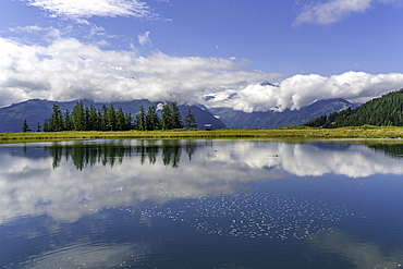 View of reflection of mountains and clouds in Plettsaukopf Reservoir on a sunny day, Bruckberg, Salzburg, Austria, Europe