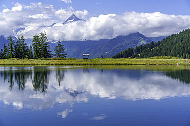View of reflection of mountains and clouds in Plettsaukopf Reservoir on a sunny day, Bruckberg, Salzburg, Austria, Europe
