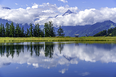 View of reflection of mountains and clouds in Plettsaukopf Reservoir on a sunny day, Bruckberg, Salzburg, Austria, Europe