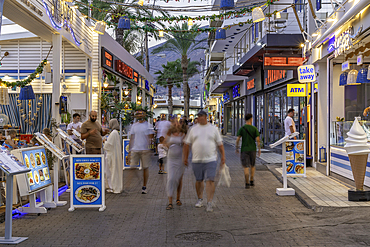 View of tavernas and shops on main street at dusk, Limenas Chersonisou, Crete, Greek Islands, Greece, Europe