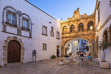 Arco Scoppa arch and Palazzo Vescovile and cafe in the Largo Arcid Teodoro Trinchera square in evening, Ostuni, Brindisi province, Puglia, Italy, Europe