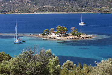 Greek Orthodox church on small island with anchored yacht off Russian Bay with crystal clear turquoise water, Poros, Saronic islands, Greek Islands, Greece, Europe
