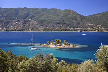 Greek Orthodox church on small island with anchored yacht off Russian Bay with crystal clear turquoise water, Poros, Saronic islands, Greek Islands, Greece, Europe