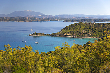 View over Paralia Zogerias beach with crystal clear blue water in bay and anchored yachts, Spetses, Saronic Islands, Greek Islands, Greece, Europe