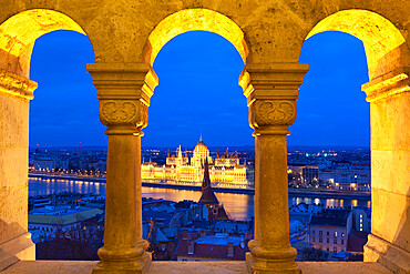 Parliament (Orszaghaz) through arches of Fishermen's Bastion (Halaszbastya) at dusk, UNESCO World Heritage Site, Budapest, Hungary, Europe