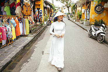 Vietnamese woman in ao dai walking down street, Hoi An, Quảng Nam Province, Vietnam