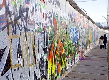 Couple walking along the East Side Gallery Berlin Wall mural, Berlin, Germany, Europe 