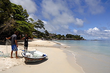 Two fishermen with boat taking fish from net on Beau Vallon beach, Mahe, Seychelles, Indian Ocean