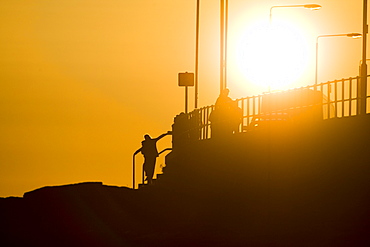 Oban esplanade with setting sun behind lamp posts and people. Oban, Argyll, Scotland, UK