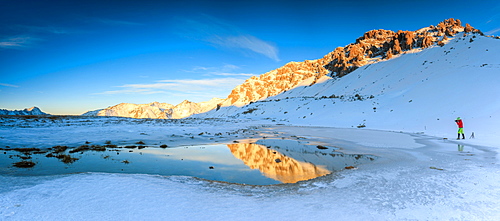 Panorama of Lake, Piz Umbrail at dawn with photographer in action framed by snow, Braulio Valley, Valtellina, Lombardy, Italy, Europe