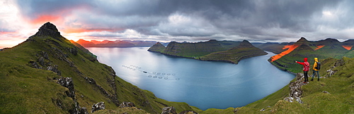 Panoramic of hikers on cliffs looking to the fjords, Funningur, Eysturoy island, Faroe Islands, Denmark, Europe