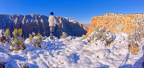 A hiker standing on a snowy cliff on the east rim of Grand Canyon National Park Arizona.