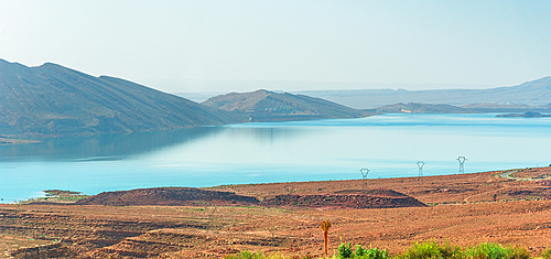 Turquoise waters of Barrage Al-Hassan Addakhil in Parc National Al Hassan Addakhil near Errachidia, Morocco, framed by arid red hills and distant mountains