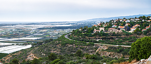 Mediterranen village with red-roof houses nestled on a hillside, overlooking farmland, the sea, and vibrant summer flora. Panoramic view. Zikhron Ya'akov, Israel.