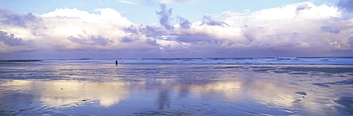 Beach at Embleton Bay with lone walker, dramatic clouds and reflections in wet sand, near Alnwick, Northumberland, England, United Kingdom, Europe