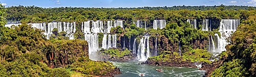 A sweeping panoramic view of waterfalls and river, lined with forest and a clear sky, The Iguazu Falls between Argentina and Brazil