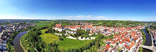 Fascinating aerial view of Donauwörth with its characteristic red roofs and historic buildings. A striking building with a tower stands out in the foreground, surrounded by well-tended green spaces and trees. The town stretches along the rolling hills and offers a picturesque atmosphere with idyllic streets, a historic townscape and expansive landscapes. Donauwörth, Swabia, Bavaria, Germany