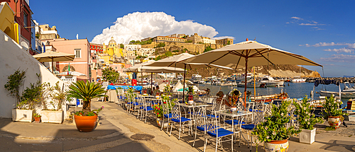 View of restaurants in Marina di Corricella and Church of Santa Maria delle Grazie in background, Procida, Phlegraean Islands, Gulf of Naples, Campania, Southern Italy, Italy, Europe