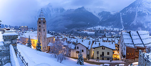 View of Church of Saint Pantalon and the snow covered town centre and mountainous background in winter, Courmayeur, Aosta Valley, Italy, Europe