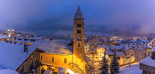 View of Church of Saint Pantalon and the snow covered town centre and mountainous background in winter at dusk, Courmayeur, Aosta Valley, Italy, Europe