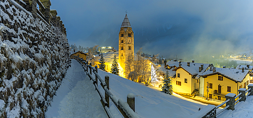 View of Church of Saint Pantalon and the snow covered town centre and mountainous background in winter at dusk, Courmayeur, Aosta Valley, Italy, Europe