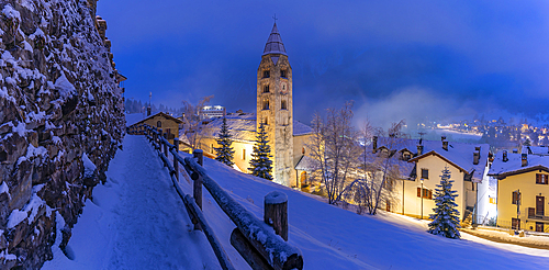 View of Church of Saint Pantalon and the snow covered town centre and mountainous background in winter at dusk, Courmayeur, Aosta Valley, Italy, Europe