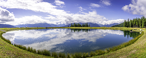 View of reflection of mountains and clouds in Plettsaukopf Reservoir on a sunny day, Bruckberg, Salzburg, Austria, Europe