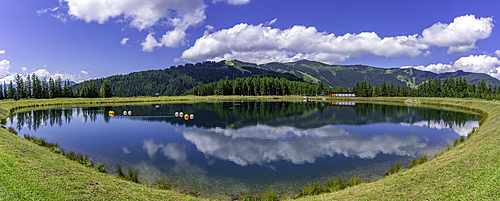 View of reflection of mountains and clouds in Plettsaukopf Reservoir on a sunny day, Bruckberg, Salzburg, Austria, Europe