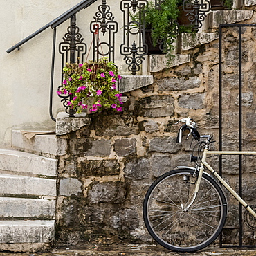 A bicycle parked beside a stone wall with steps leading up and plants decorating the railing, Budva, Opstina Budva, Montenegro