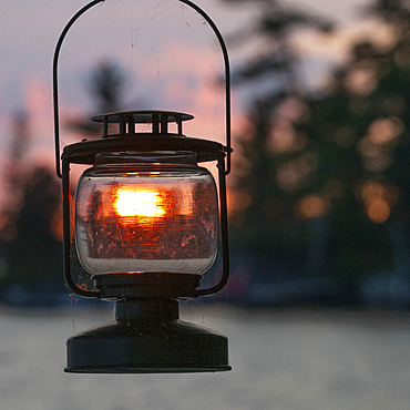 Sunset light glows and illuminates the glass of a black metal lantern, Lake of the Woods, Ontario, Canada