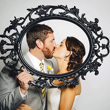 Caucasian bride and groom kissing behind empty frame