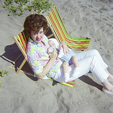 Caucasian mother sitting on beach feeding bottle to baby son