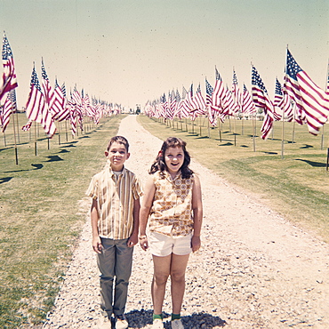 Caucasian brother and sister holding hands near American flags