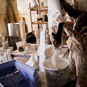 Caucasian artist pouring plaster mix into bucket