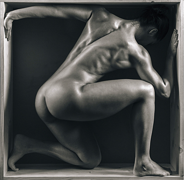 Naked muscular Mixed Race crouching in box