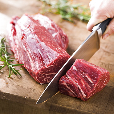 Knife cutting beef tenderloin on wooden table