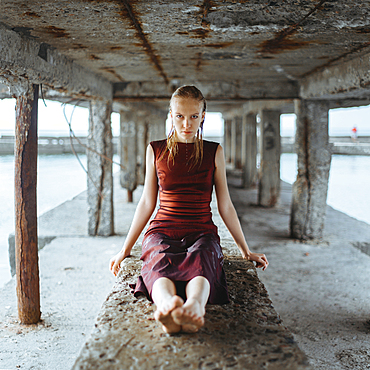 Caucasian girl wearing wet dress sitting underneath dock