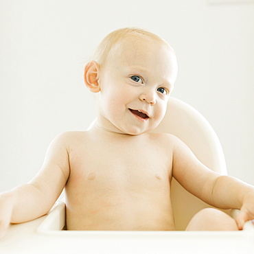 Portrait of shirtless baby boy (12-17 months) sitting in high chair