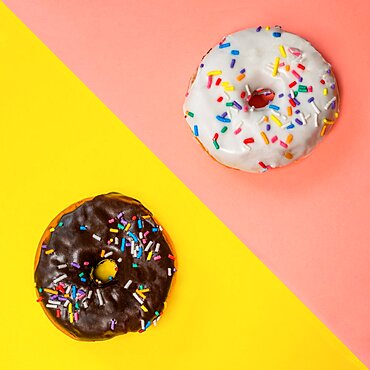 Overhead view of two donuts with icing and sprinkles on multi-colored background