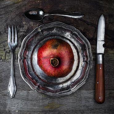 Food photography, still life, pomegranate on old plate and cutlery, from above, studio shot, symbol photo