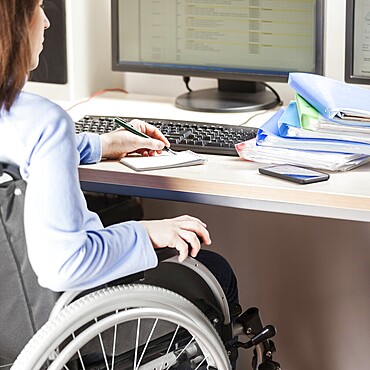 Invalid or disabled young business woman person sitting wheelchair working office desk computer