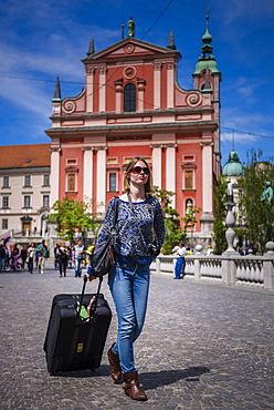 Tourist with suitcase, walking past the Franciscan Church of the Annunciation in Preseren Square, Ljubljana, Slovenia, Europe