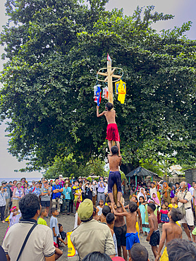 Boys working together to climb a greased pole to get to prizes at the top on Sumbawa Island, Indonesia.