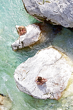 Two young women sitting on rocks in the river Soca, Alpe-Adria-Trail, Tolmin, Slovenia