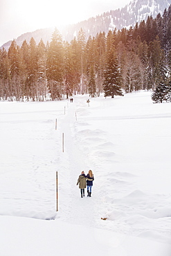 Two young women walking in snow, Spitzingsee, Upper Bavaria, Germany