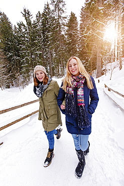 Two young women arm in arm walking in snow, Spitzingsee, Upper Bavaria, Germany