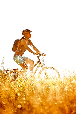 Young woman riding her bike near a meadow on a sunny day, Tannheimer Tal, Tyrol, Austria