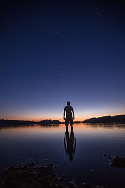 Young man standing in a lake at night, Freilassing, Bavaria, Germany